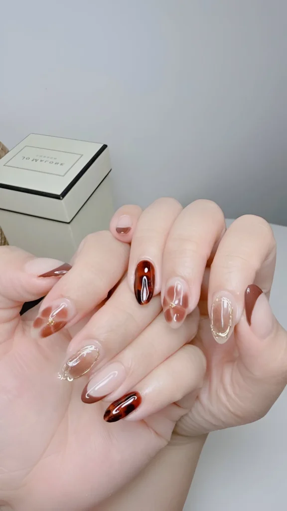Abstract coffee-toned design with translucent brown patches and tips, accented by fine gold lines on oval nails – sophisticated classy nail ideas.