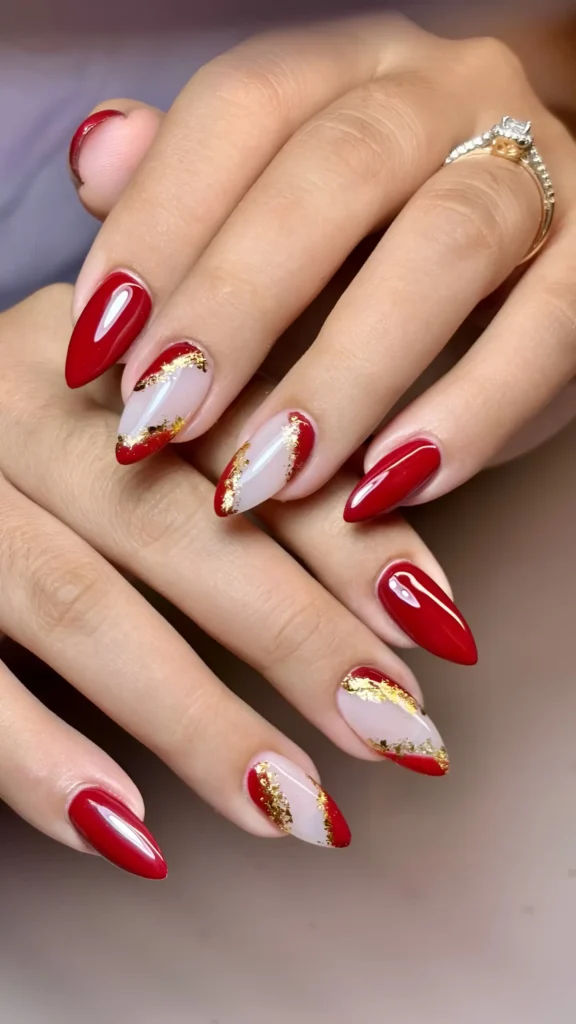 Almond-shaped nails with deep red polish and abstract red tips edged with gold leaf foil.