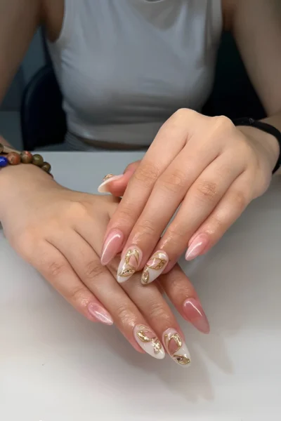Long almond nails with a sheer base featuring prominent 3D sculptural gold metallic abstract art details.