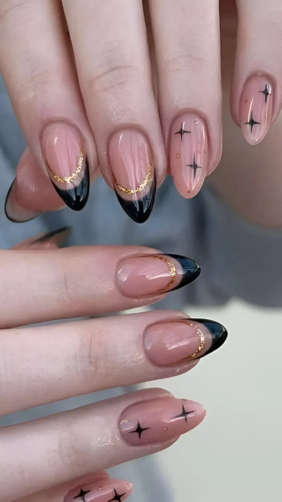 Almond nails with mixed celestial design: black French tips with gold crescent accents, and sheer nails with black starbursts and gold dots.