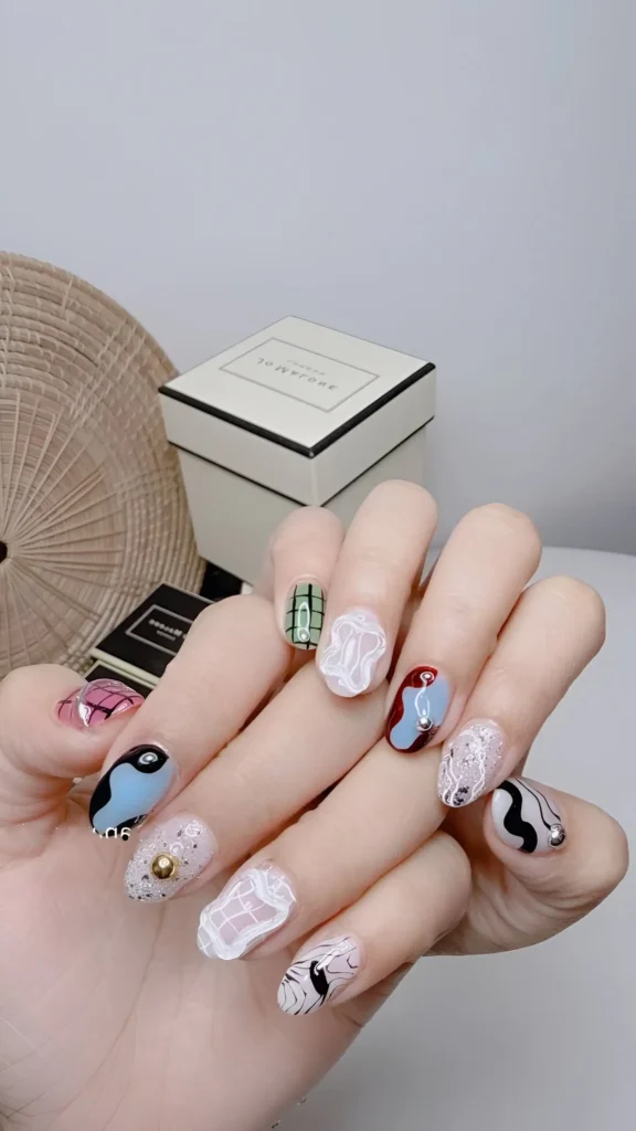 Curated abstract nail art set on short nails featuring swirls, color blocking, textures, and metallic details.