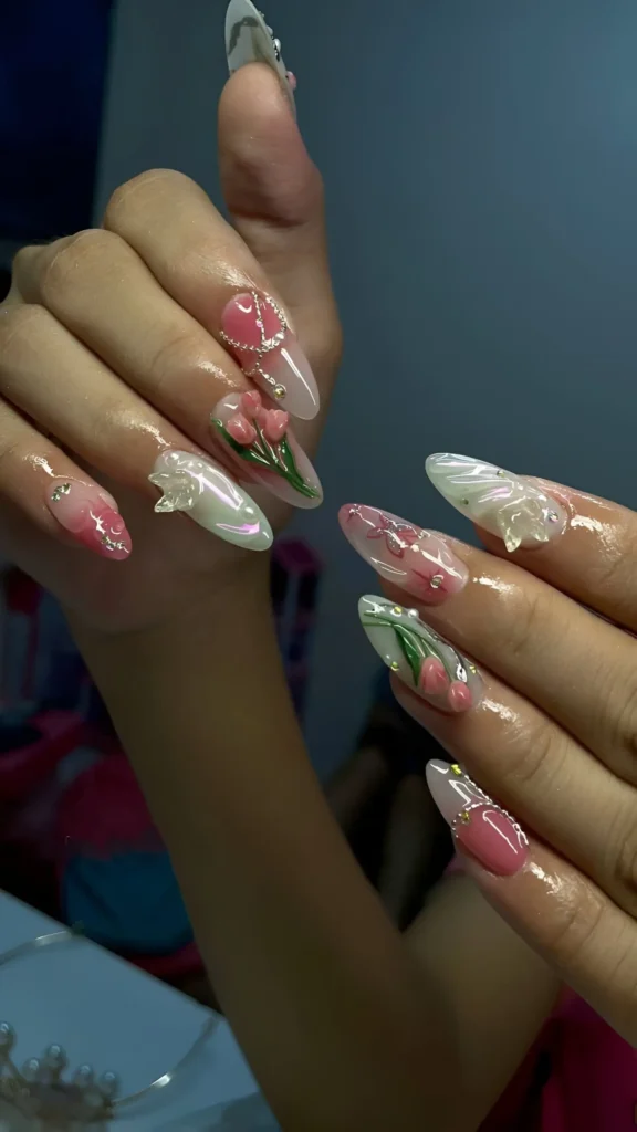 Long stiletto nails featuring painted pink tulips, pink color blocks outlined in crystals, and dimensional pearly white sculpted accents.