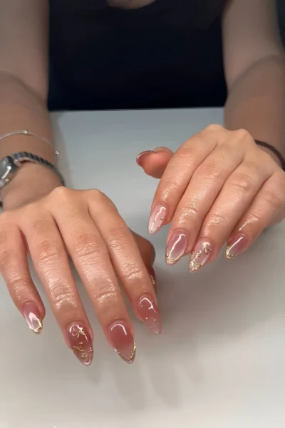 Almond nails with a sheer base featuring delicate gold swirl line art and fine gold metallic tips.