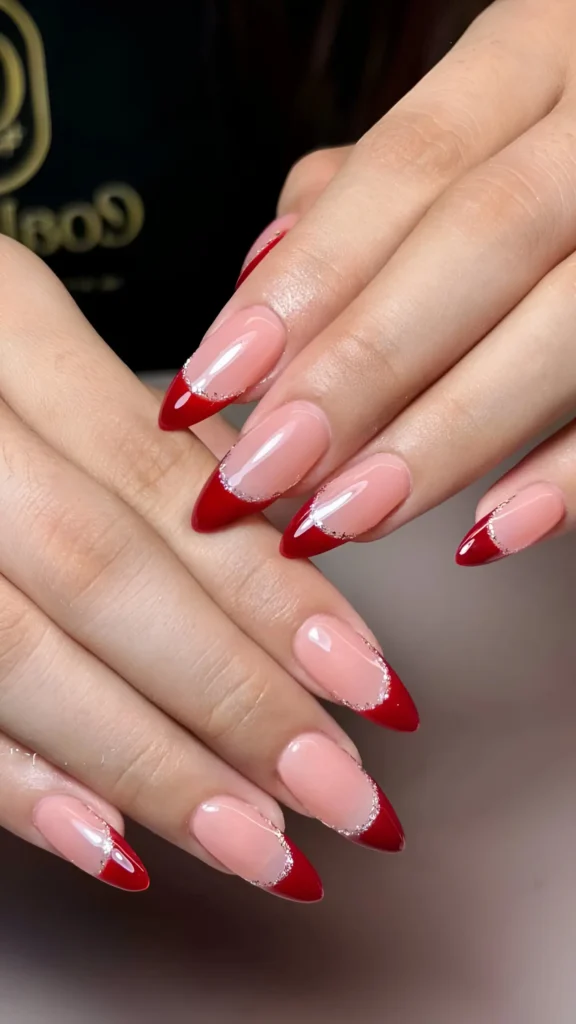 Almond nails with sheer base, deep red V-shaped French tips, and silver glitter outline.