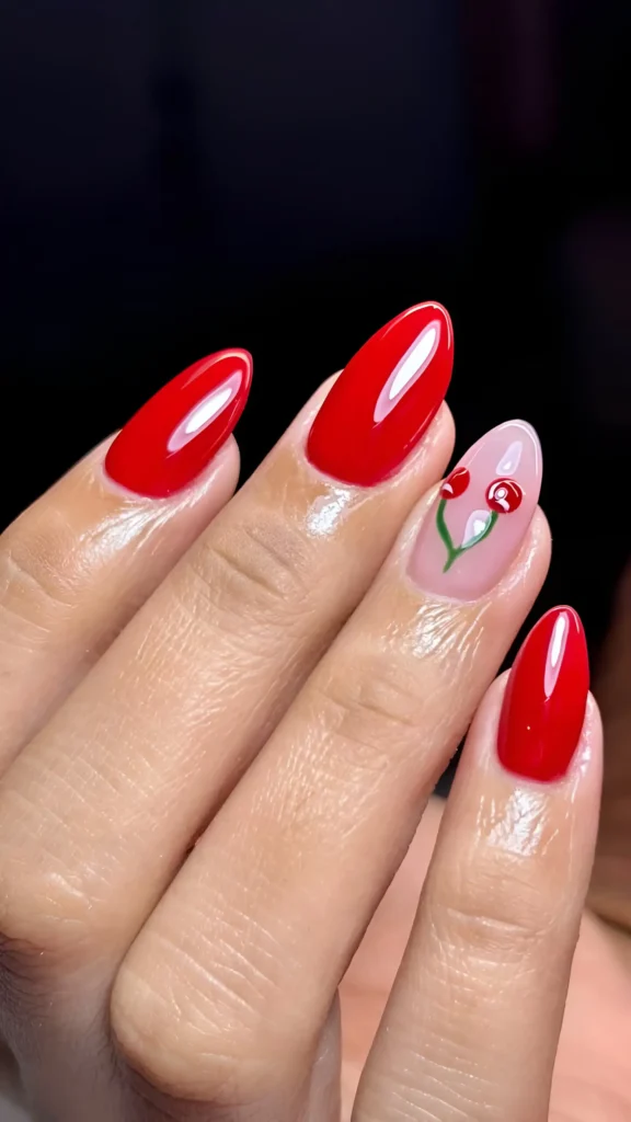 Almond nails with glossy bright red polish and a single accent nail featuring cherry art on a sheer base.