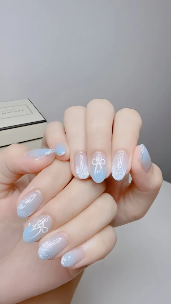 Ethereal sky blue shimmer polish applied with a gradient effect and white bow line art on almond nails.