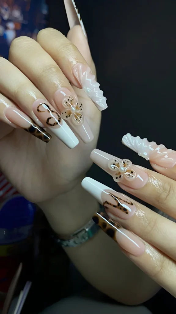 Long coffin nails with sheer nude base featuring tortoiseshell tips, white tips, dimensional white waves, abstract lines, and dotted floral motifs with pearls.