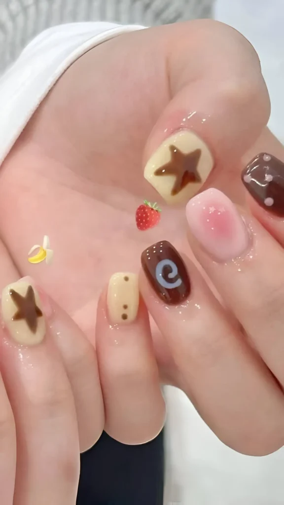 Very short nails with a mix-and-match dessert theme: creamy base nails with brown stars and dots, solid brown nails, and a pink blush nail.