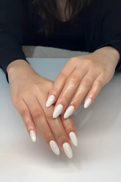 Medium-length almond nails painted with a glossy opaque milky white polish, a modern clean look.