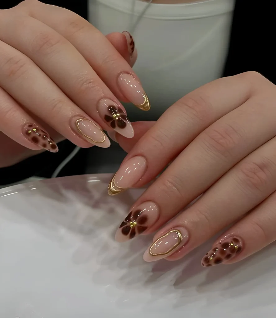 Almond nails mixing sheer nude base with tortoise shell patterns/dark florals with gold beads, and gold metallic outlines.