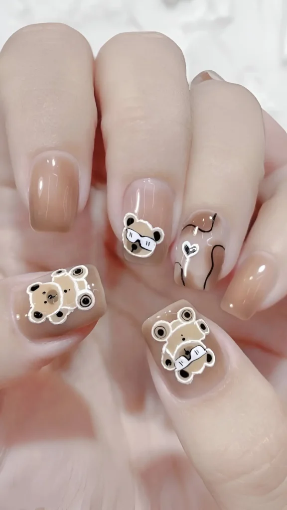 Cute short nail design featuring a brownish-nude base with trendy teddy bear illustrations, abstract brown lines, and solid color nails.
