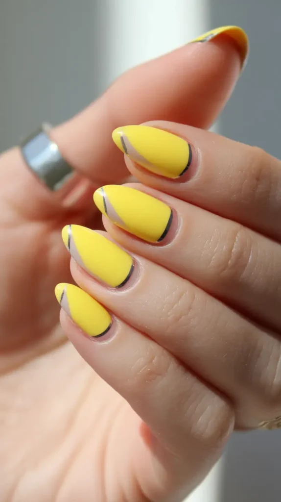 Almond-shaped nails with a matte bright yellow polish, featuring a curved negative space section along one side outlined by a thin black line.