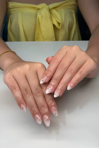 Almond nails with a soft ombré French base featuring scattered delicate silver sparkle starburst accents.