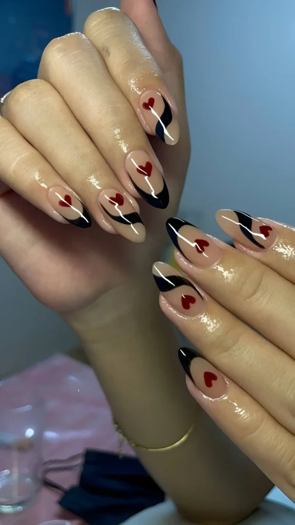 Almond nails with a sheer nude base featuring bold black abstract swirl lines and small classic red heart accents.