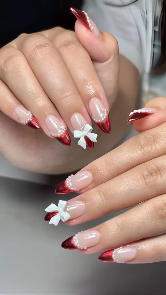 Pointed nails with metallic red V-tips outlined in pearls, and accent nails with large white 3D bows.