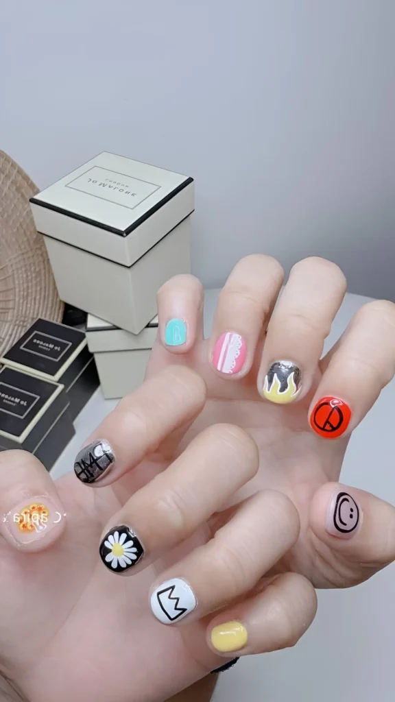 Short nails displaying varied pop art icons (daisy, crown, smiley) on different coloured backgrounds.