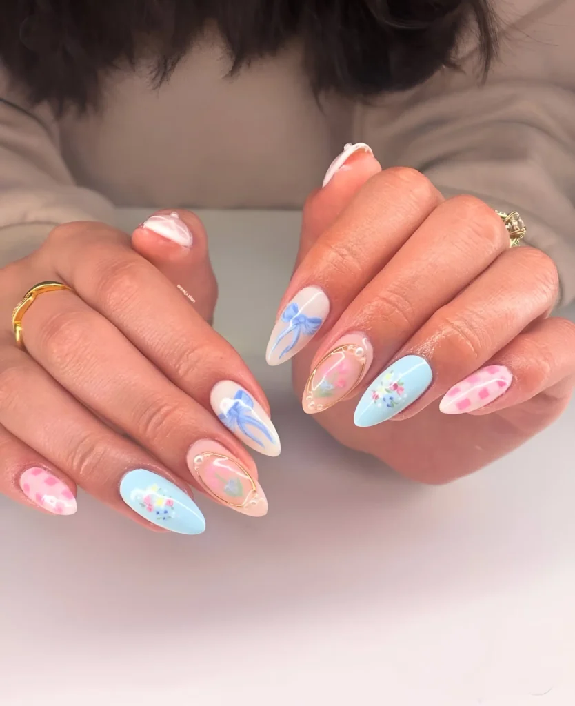 Almond nails mixing pastel blue and pink gingham patterns, painted blue bows, delicate florals, and gold outline details.