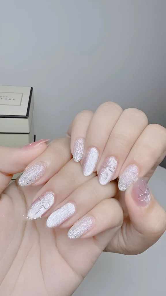 Glamorous almond nails fully coated in dense, fine silver glitter creating a sugar-spun effect, featuring a subtle bow design.