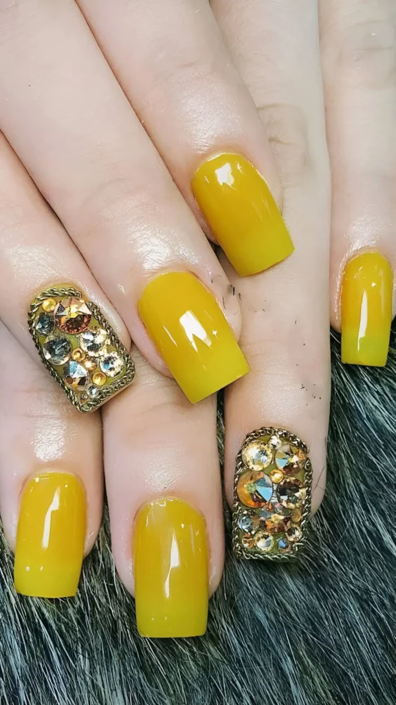 Medium square nails with solid golden yellow polish mixed with accent nails fully encrusted with large, faceted golden/iridescent gems bordered by gold trim.