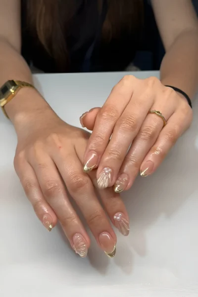 Almond nails with a sheer base featuring 3D clear seashell textures, fine gold tips, and pearl accents.