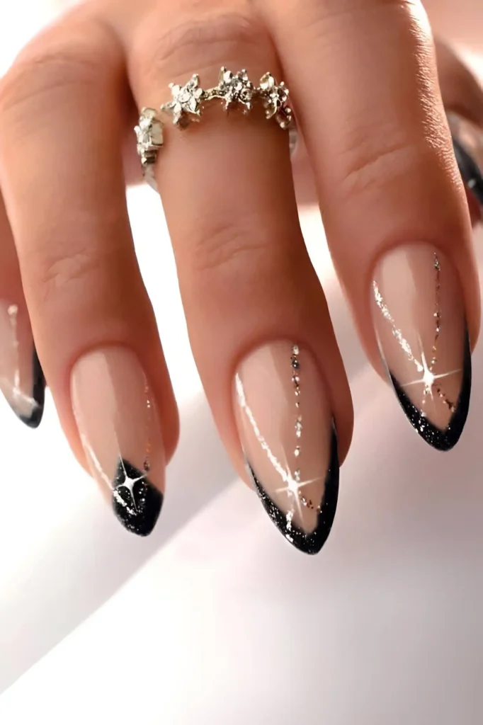 Almond nails with black glitter French tips and sheer bases decorated with silver glitter lines and starburst accents.