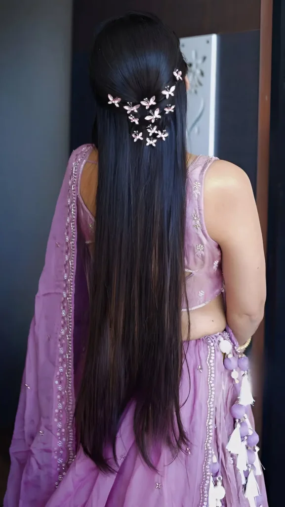 Back view of long straight dark hair in a sleek half-up style adorned with a cascade of small metallic butterfly clips.