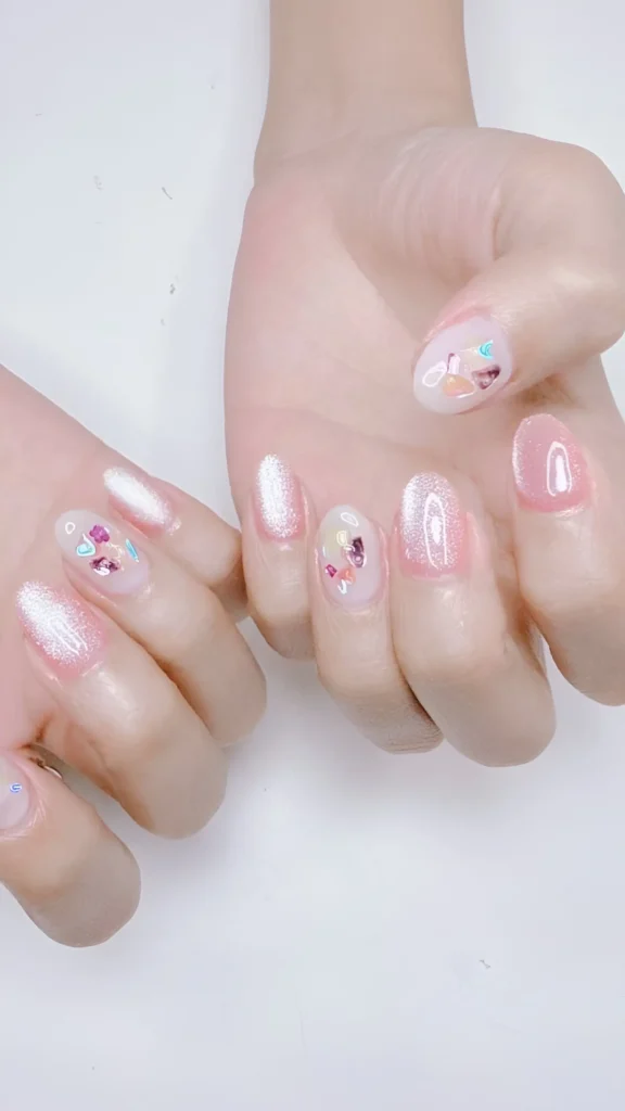 Chic nail look mixing luminous pearlescent polish with accent nails featuring embedded chunky iridescent glitter shards.