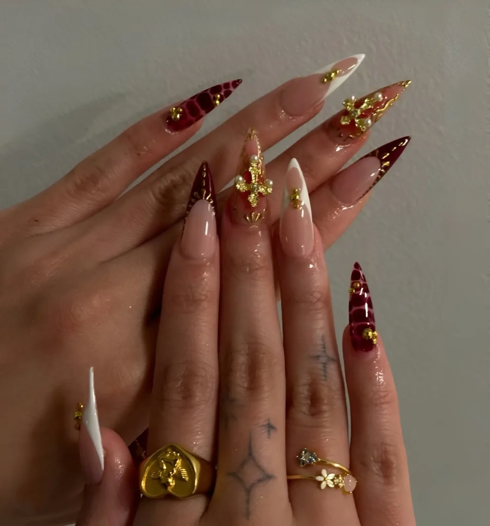 Gothic glam stiletto nails featuring deep V-tips and large, ornate gold 3D cross charms with gems.