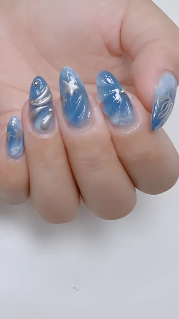 Artistic blue and white marbled almond nails adorned with sculpted 3D silver waves and star charms.