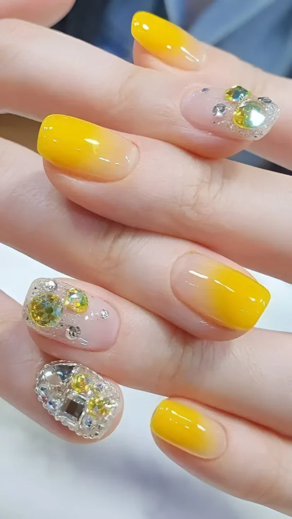 Medium square nails featuring a mix of yellow ombré (fading from yellow tips to sheer base) and accent nails densely covered in yellow and clear faceted gems.