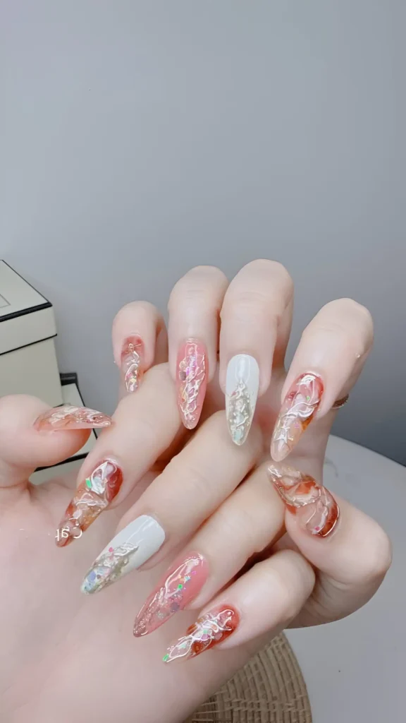 Ornate filigree-style nail art: dimensional metallic and coloured swirls over neutral bases on long stiletto nails.