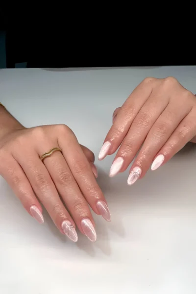 Almond nails with a luminous pearlescent white finish featuring subtle clear 3D bow accents.