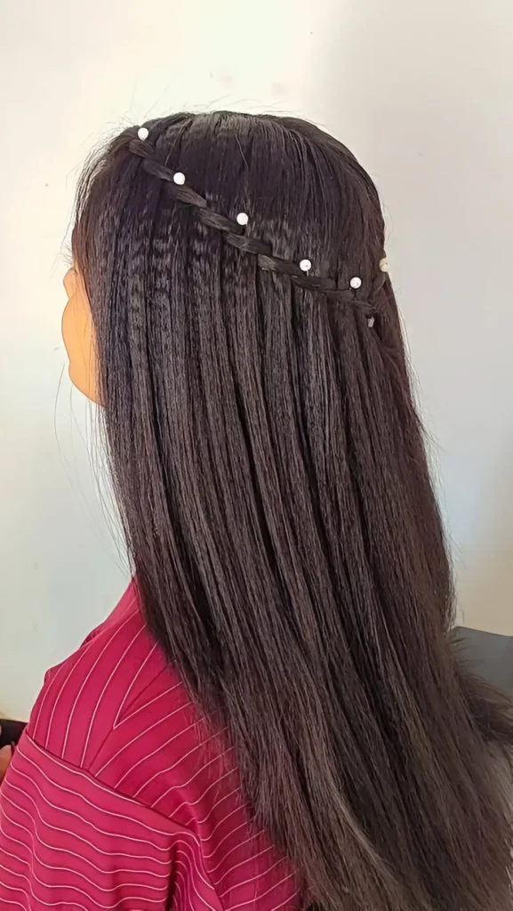 Back view of long dark crimped hair featuring a thin headband braid across the crown adorned with small white pearls.