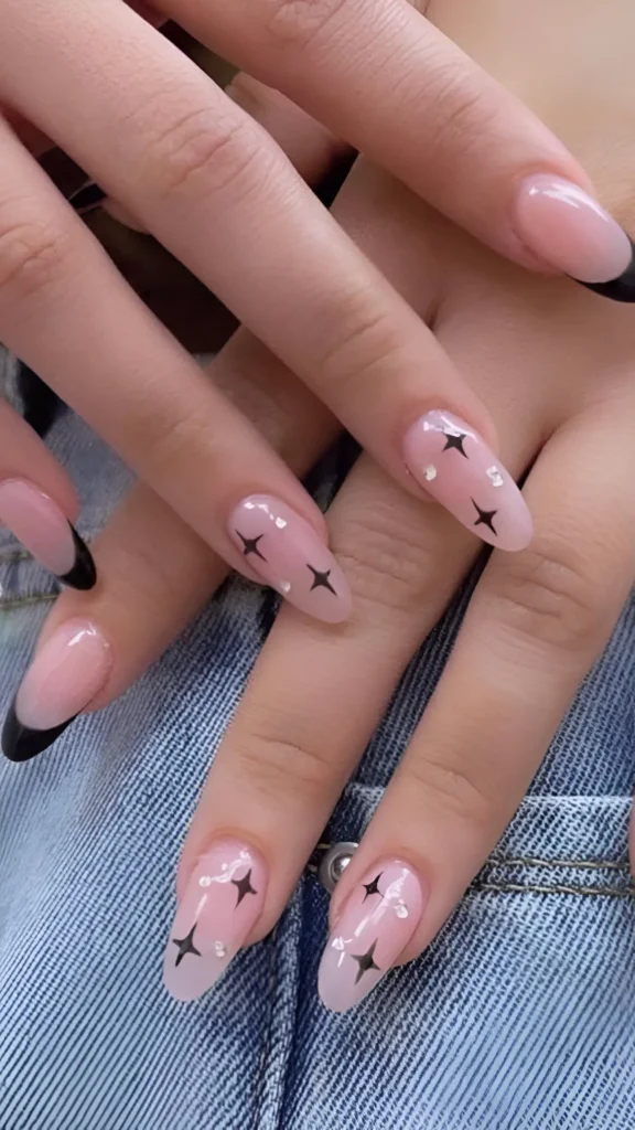 Almond-shaped nails with a mixed design: classic black French tips and sheer nails decorated with black starburst graphics and tiny accents.