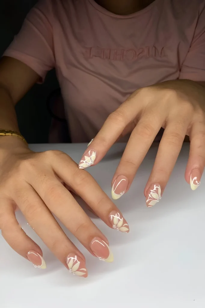 Almond summer nails with sheer base, pale yellow French tips, and white lotus flower nail art.