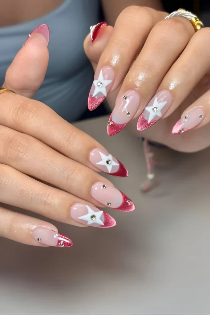 Long stiletto nails with pink glitter V-tips, accent white stars with gem centers, and scattered rhinestones.