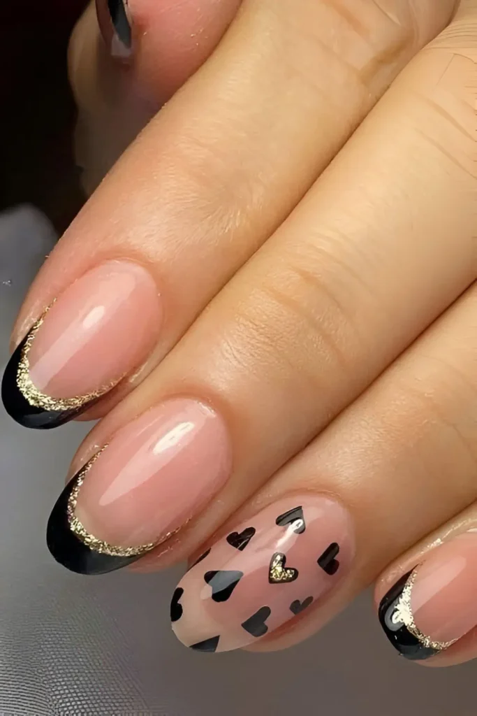 Rounded nails with mixed design: black French tips with gold crescent outlines, and a sheer accent nail with multiple black hearts and one gold heart.