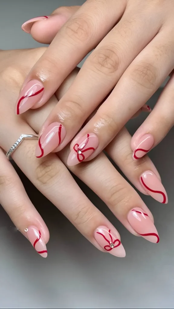 Pointed almond nails with sheer base featuring delicate red line art including swirls and bow outlines with gem centers.