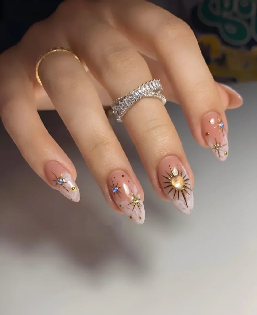 Ethereal almond nails with gold celestial starbursts centered with gems over a cloudy white and sheer nude base.