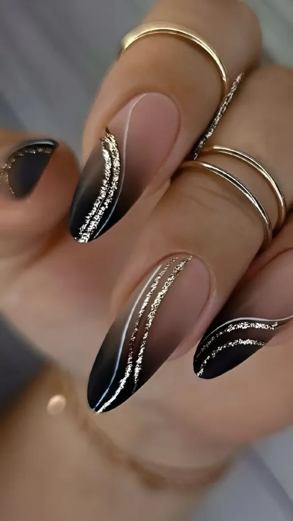 Almond nails featuring a sheer-to-black ombre gradient background adorned with curved lines of textured gold glitter.