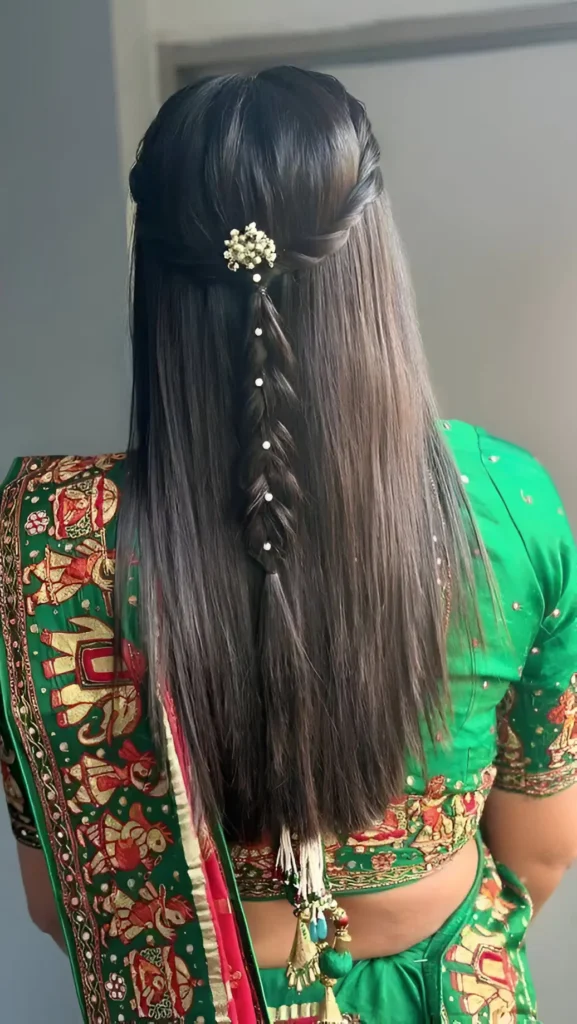 Back view of long straight dark hair in a half-up style featuring a floral accessory and a thin central braid adorned with pearls.