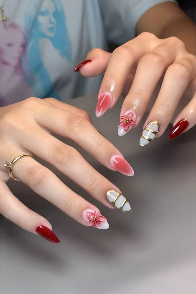 Mixed nail art on pointed nails including solid red, white with gold bands, red aura effect, and red floral designs.