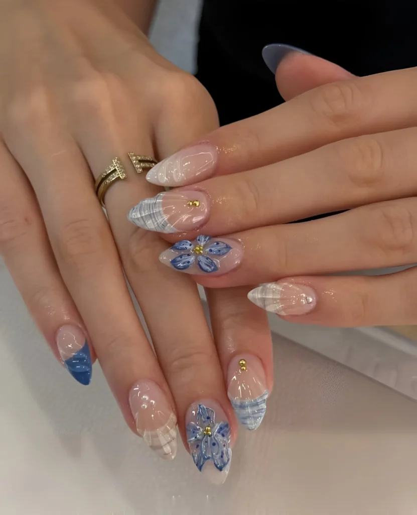 Almond nails mixing blue and white plaid patterns, blue 3D flowers with white details, and a solid blue V-tip French on a sheer base.