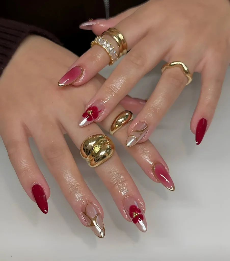 Luxurious long nails combining deep red polish, metallic gold tips, abstract gold lines, and red floral details.