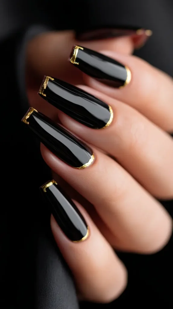 Close-up of long, glossy black nails featuring a textured gold accent along the cuticle line.