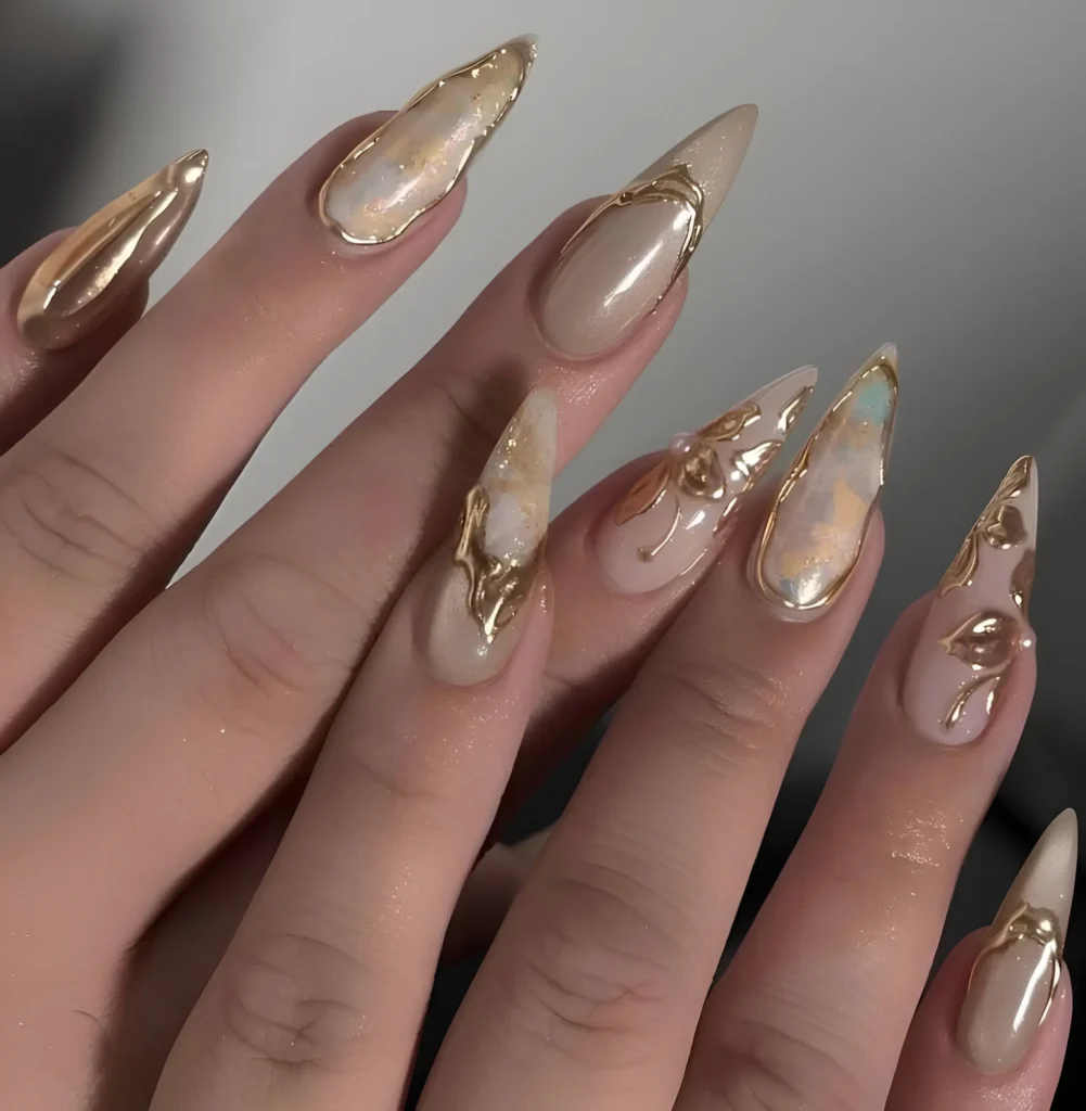 Baroque stiletto nails featuring ornate sculpted gold frames and details over textured pearlescent white/pink bases.