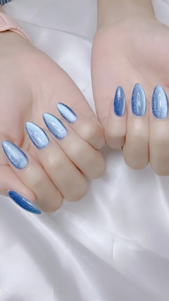 Almond nails featuring a dusty blue magnetic polish creating a sleek, silvery-blue velvet cat-eye effect. A trendy classy nail idea.