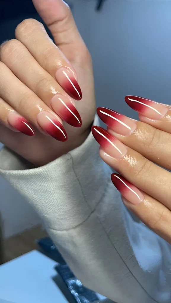 Pointed almond nails featuring a classic ombré gradient from sheer nude at the base to deep oxblood red at the tips.