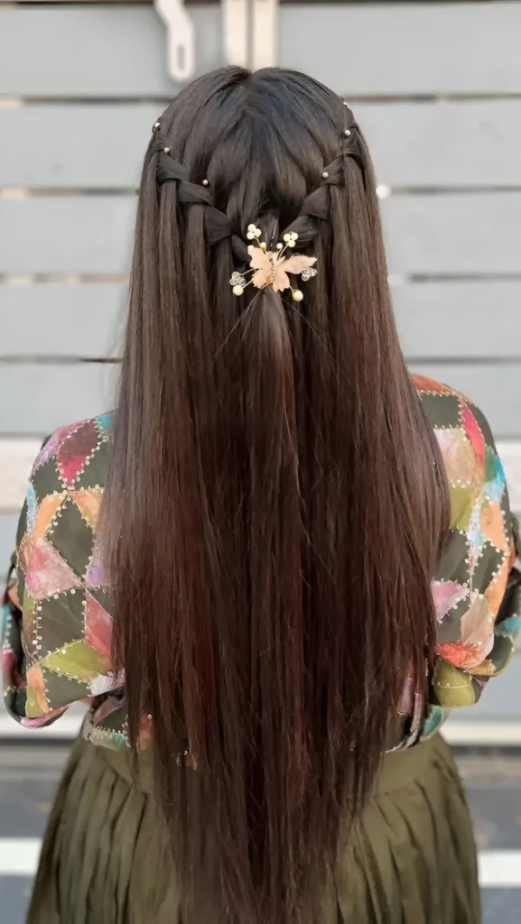 Back view of long straight dark hair styled in a half-up look with gold bead-accented braids meeting under a gold butterfly clip.
