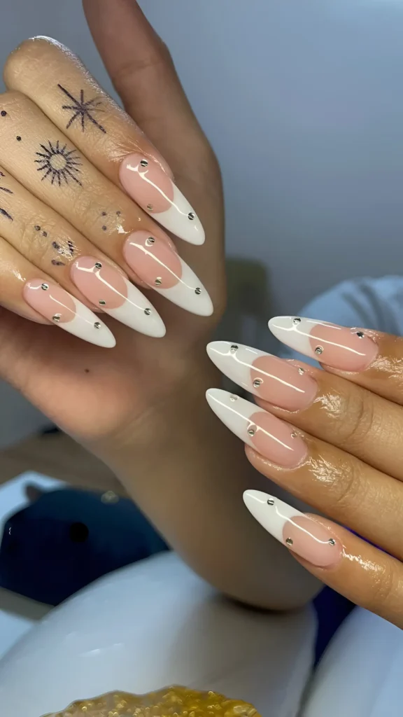 Almond nails with sheer pink base and deep white French tips accented with small silver studs along the smile line.